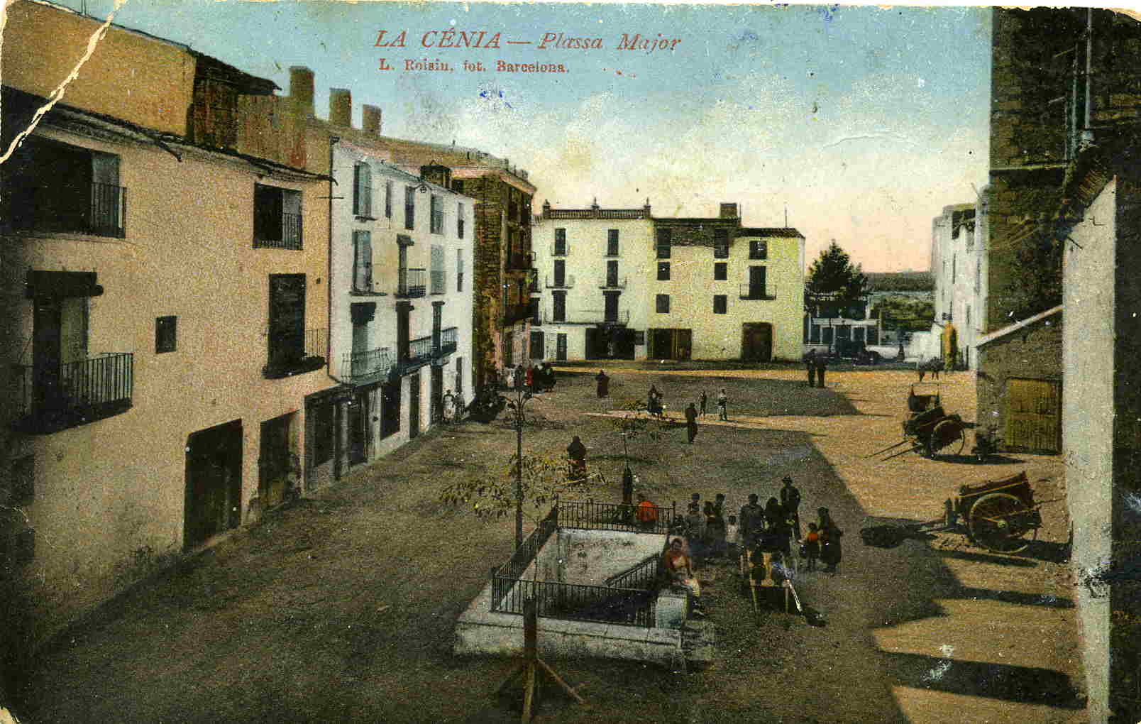 Vista de la pla&ccedil;a Major de la S&eacute;nia. Fixeu-vos amb el carro per portar els c&agrave;nters que hi ha a la vora de la Font Vella. Principis segle XX. Font: Fons Lucien Roisin &ndash; Centre d&rsquo;Estudis Seniencs.